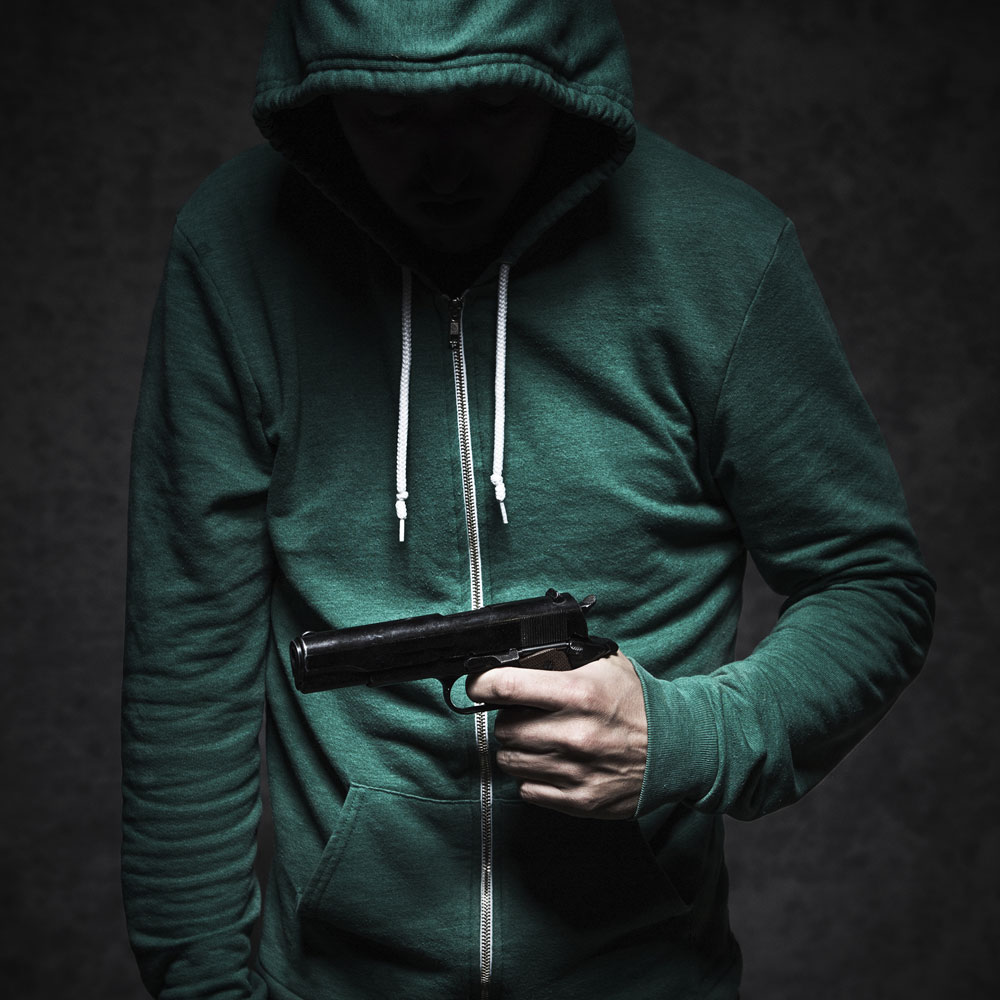 Young man in green hoodie looking at gun in hand